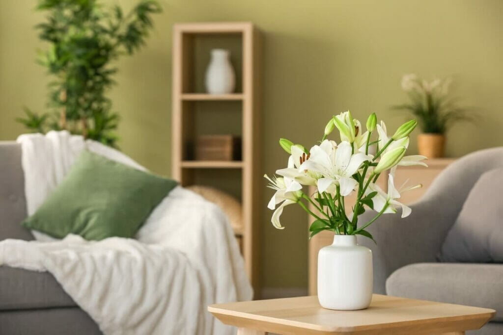 A vase of white lily flowers on a small wooden side table in a living room