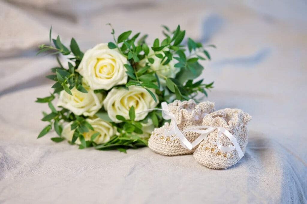 A small bouquet of yellow roses next to small knitted boots for a new baby
