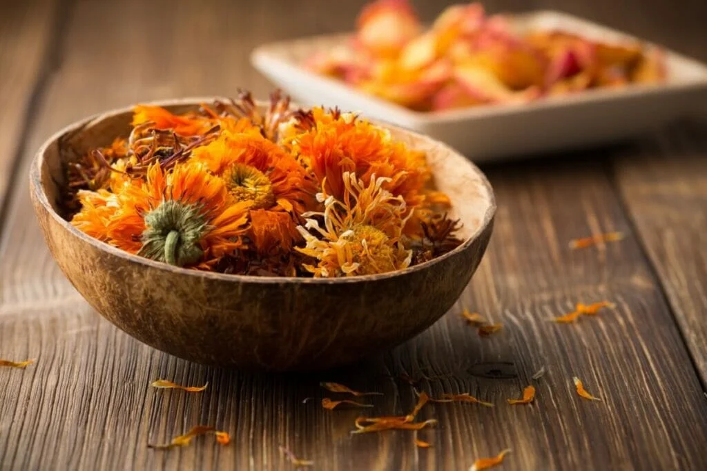 A bowl of dried marigold heads sit in a bowl on a wooden table
