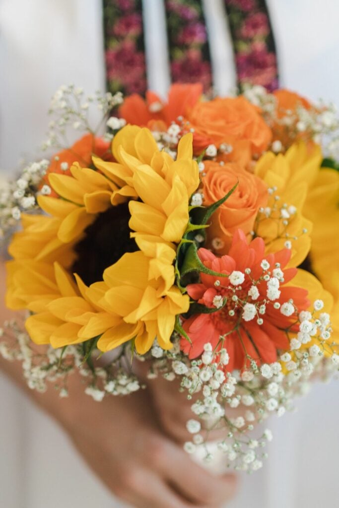 Bright sunflower bouquet mixed with orange roses, red daisies, and Baby’s Breath, capturing vibrant countryside charm.