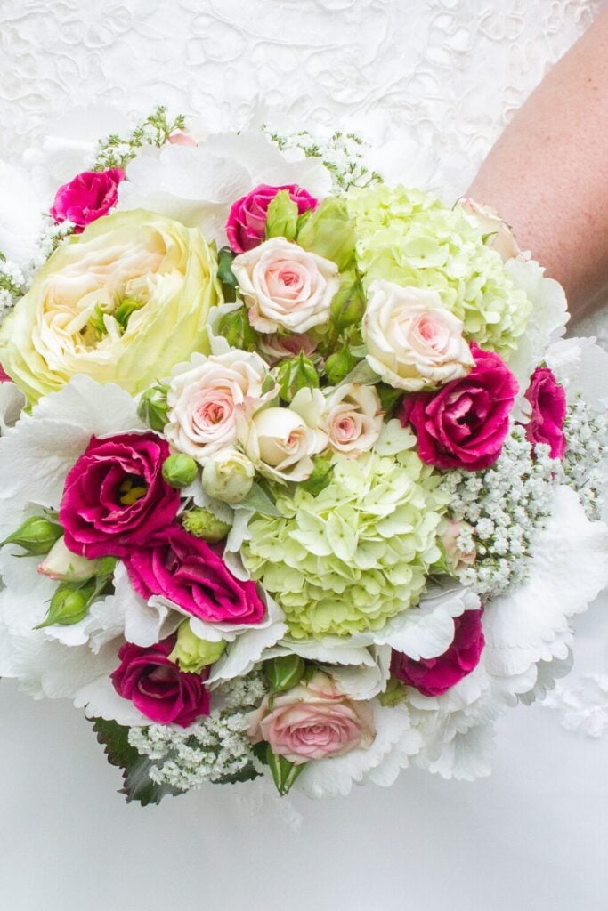 Wedding bouquet featuring green hydrangeas, cream garden roses, magenta flowers, and Baby’s Breath for a vibrant and elegant design.