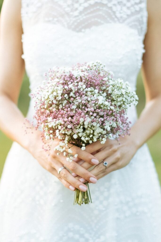 Small bridal bouquet of pink and white baby's breath held against white wedding dress