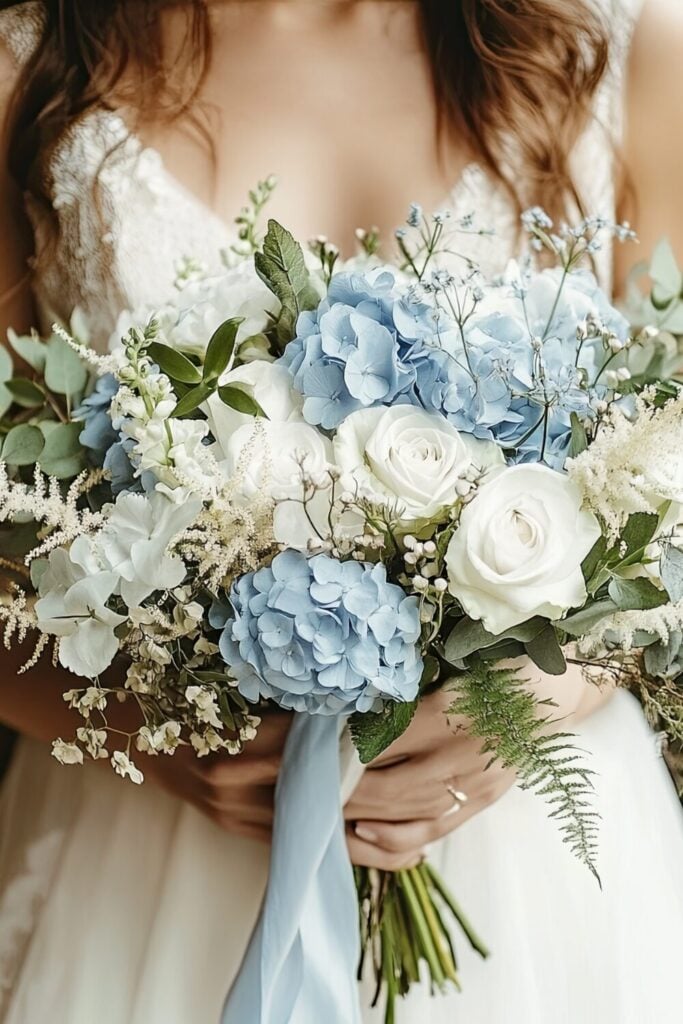 A wedding bouquet featuring soft white roses with delicate blue hydrangeas and lush greenery